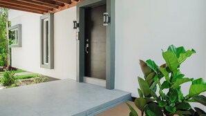 Une façade moderne avec un patio en béton, une pergola en bois et une porte dotée d’un cadre gris.