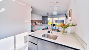 Une cuisine moderne dotée d’un grand évier, un coin repas avec une table et des chaises, et une chambre à coucher avec deux lits et une fenêtre.