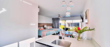 A modern kitchen with a large sink, a dining area with a table and chairs, and a bedroom with two beds and a window.