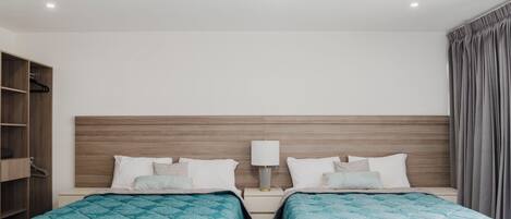 Une chambre d’hôtel avec deux lits, une tête de lit en bois, un ventilateur de plafond, une table de chevet avec une lampe et une armoire.