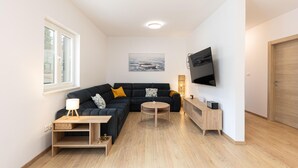 Un salon moderne comprenant un canapé d’angle, une table basse, un téléviseur fixé au mur et une fenêtre laissant entrer la lumière naturelle.