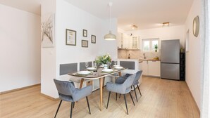Une cuisine moderne avec des meubles blancs, un réfrigérateur en acier inoxydable et un coin repas comprenant une table en bois et des chaises à revêtement gris.