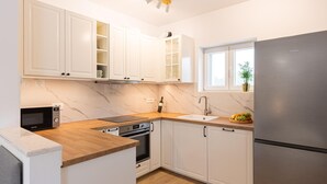 Une cuisine moderne avec des meubles blancs, un réfrigérateur en acier inoxydable, un four à micro-ondes et un four encastré.