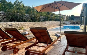 A poolside area with lounge chairs and a large umbrella. - Stunning home in Zadvarje (Zadvarje)