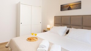 Une chambre d’hôtel avec un lit, une table de chevet avec une lampe, un plateau avec des croissants et des verres de jus de fruits, et un tableau accroché au mur.