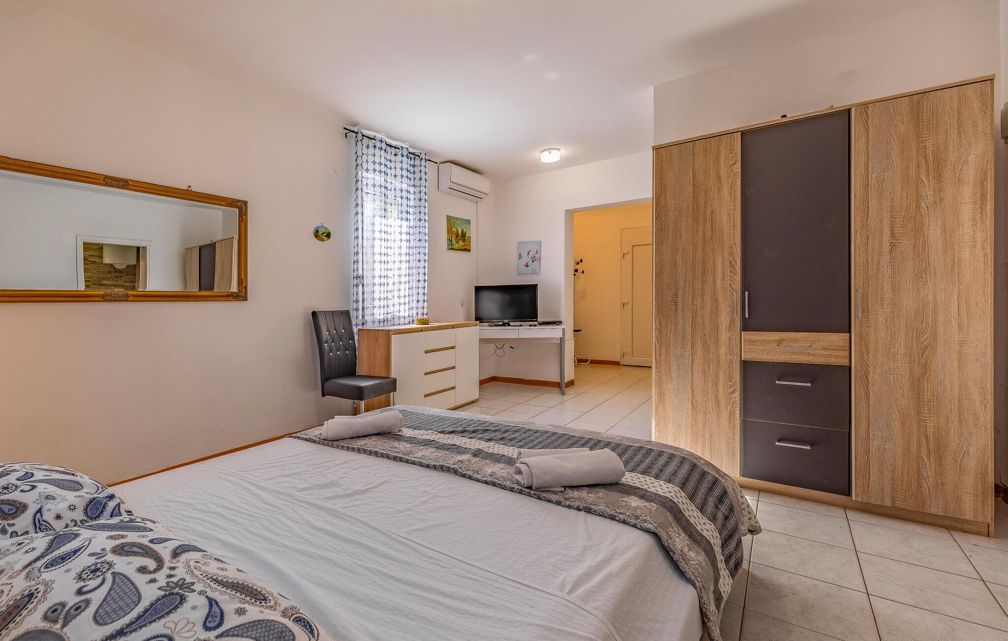 Ein Schlafzimmer mit Bett, Schreibtisch, Fernseher, Kleiderschrank und einer Badezimmertür.