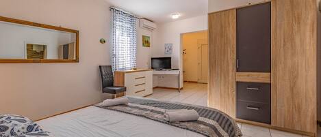 Ein Schlafzimmer mit Bett, Schreibtisch, Fernseher, Kleiderschrank und einer Badezimmertür.
