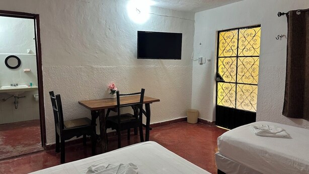 Une chambre comprenant un lit, un bureau avec une chaise, un téléviseur fixé au mur et une fenêtre agrémentée d’un paravent décoratif.