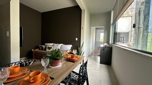 A dining area with a wooden table set for four, a sofa with cushions, and a potted plant.