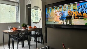 A dining area with a TV displaying a colorful scene, a round mirror, and a table set with orange plates and glasses.