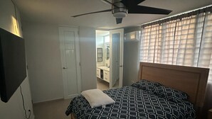 Ein Schlafzimmer mit einem Bett, Deckenventilator und Blick ins Badezimmer.