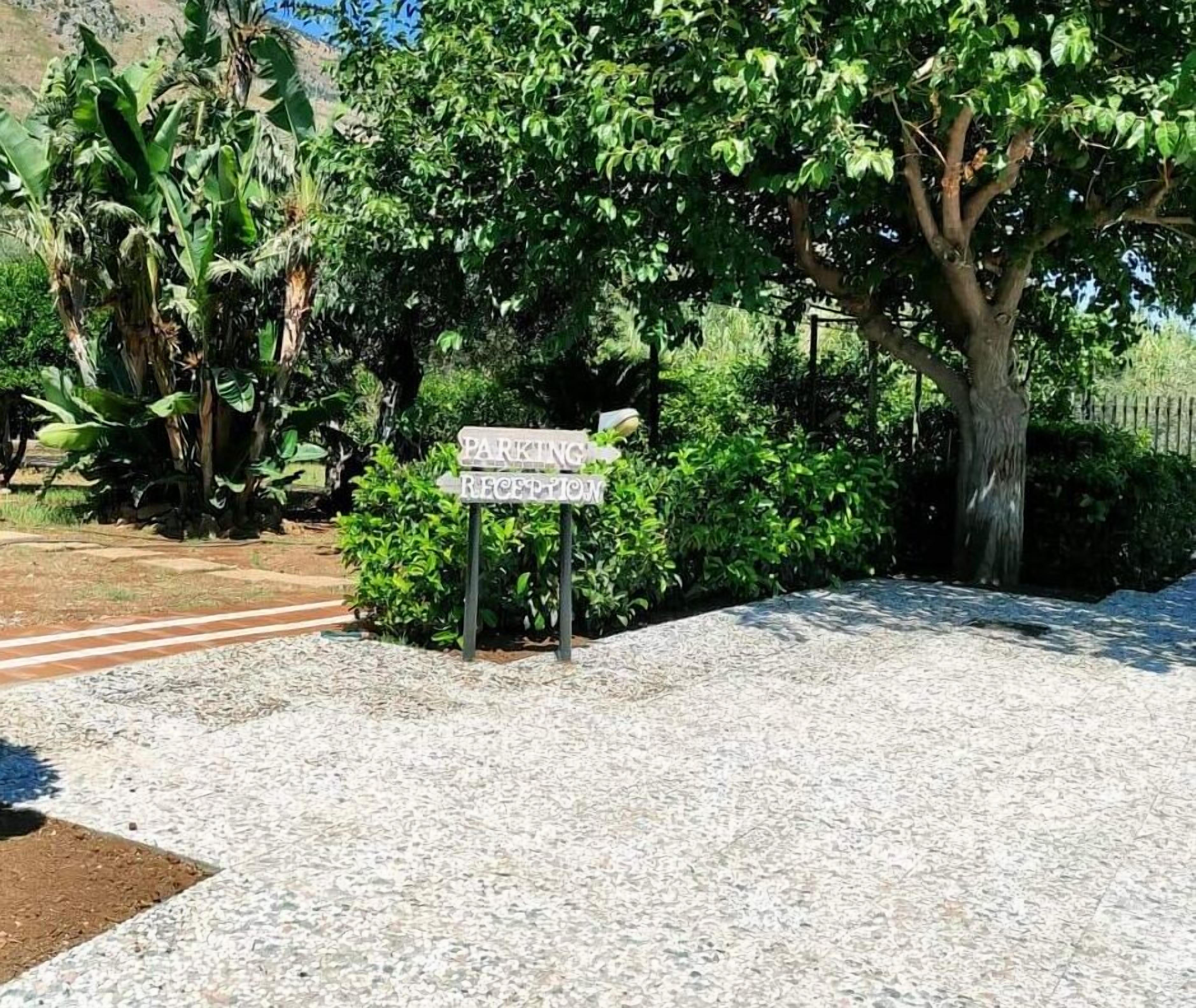 Señal que indica zona de estacionamiento y recepción, rodeada de vegetación exuberante y árboles.