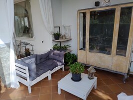 Un sofá blanco con cojines, una pequeña mesa blanca con una planta en maceta y un mueble de madera con puertas de cristal.