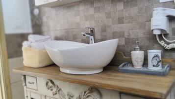 Un baño con un lavabo blanco tipo recipiente, un mueble de tocador de madera, un perchero y un secador de pelo.