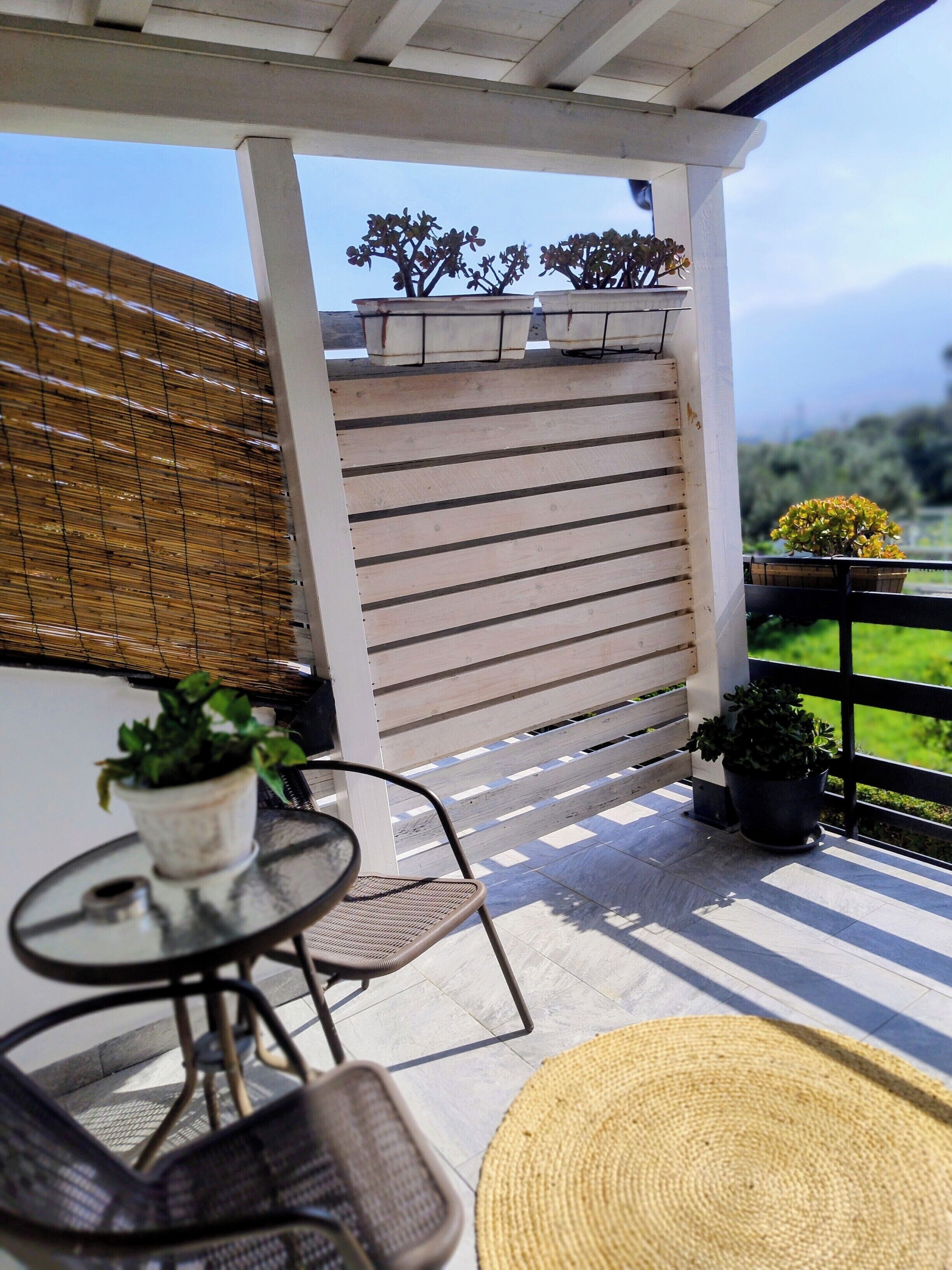 Un espacio de estar al aire libre cubierto, con una mesa, sillas, plantas en macetas y vistas a la vegetación.