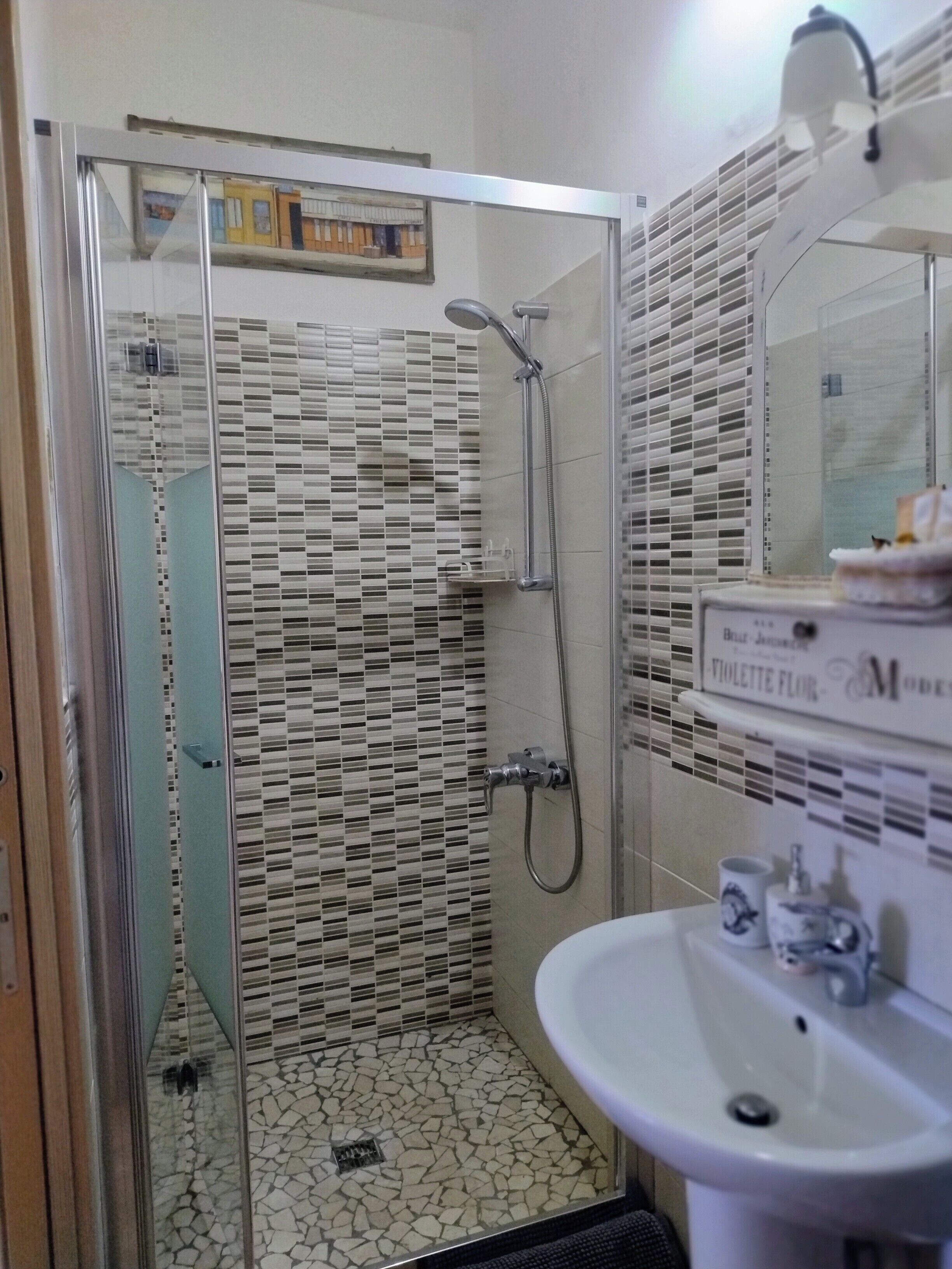A bathroom with a shower, tiled floor, and a sink with a mirror above it.