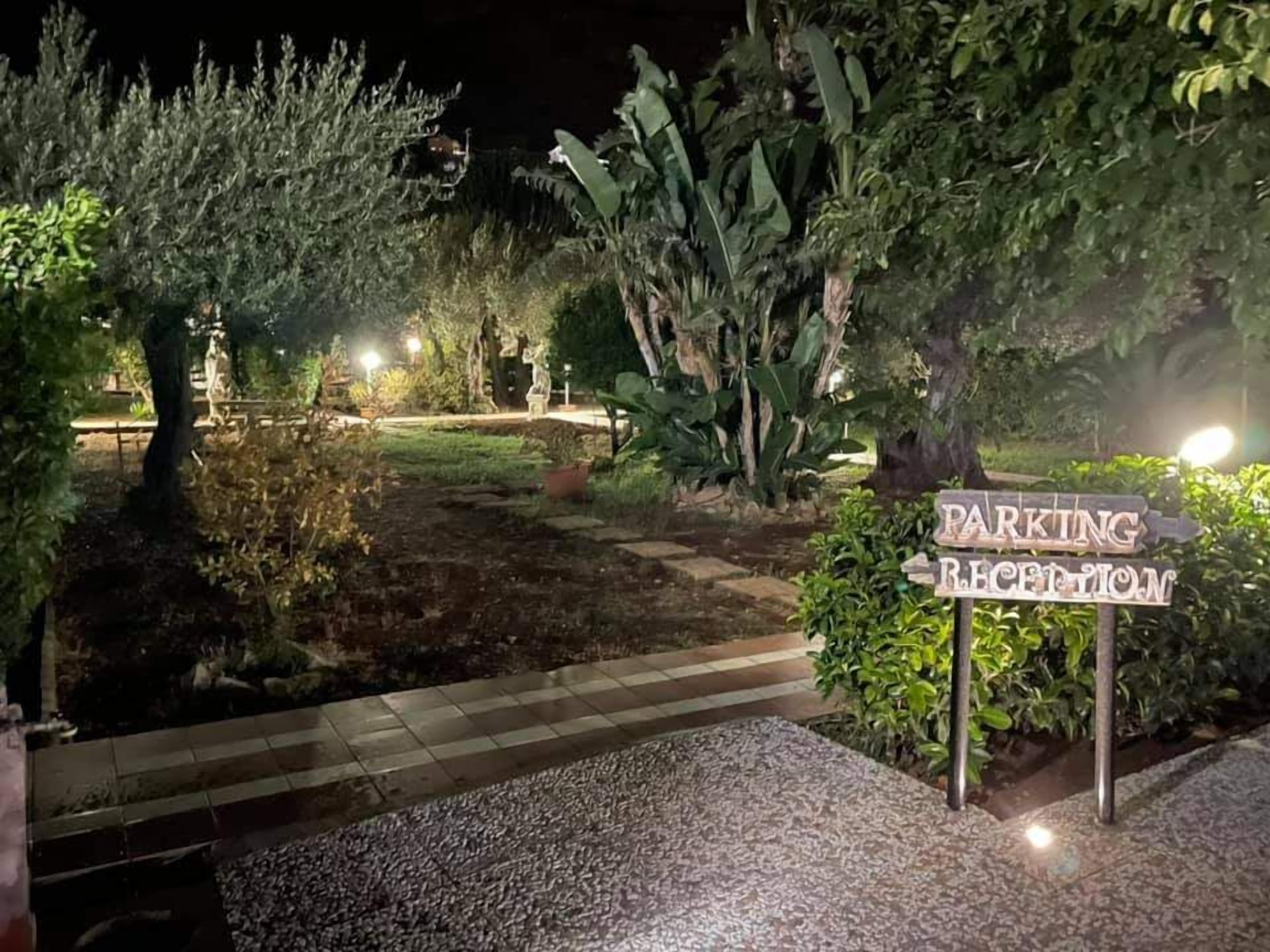 A nighttime parking reception area with a sign, paved walkway, and surrounding greenery.