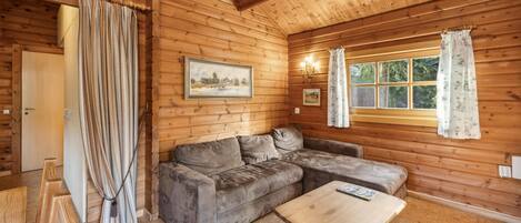 A cozy log cabin room with a sofa, a wooden coffee table, and a window with curtains.