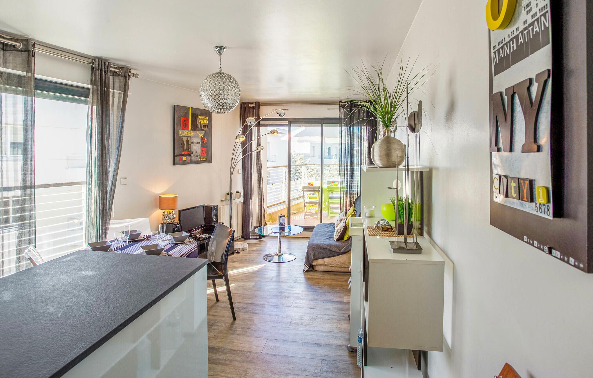 A modern living room with a dining area, a large window, and a view of the outside balcony.