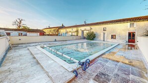 A swimming pool with a stone deck, a red door, and a stone building in the background. - Pet friendly home in NERE (NERE)