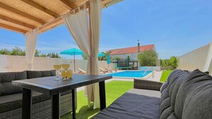 Terrassa exterior amb piscina, taula amb begudes i zona de seients coberta.