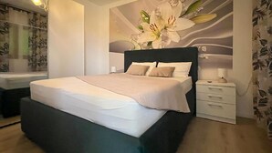 Un dormitori modern amb un llit gran, una tauleta de nit i una làmpada penjada a la paret.
