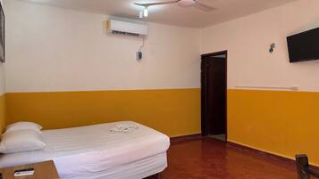 A room with a bed, a ceiling fan, an air conditioning unit, a television mounted on the wall, and a door.