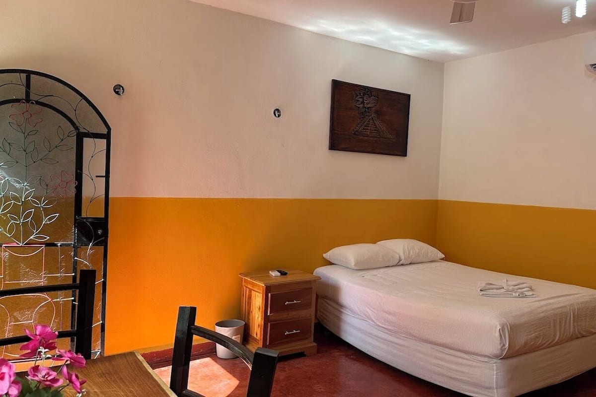 A bedroom with a bed, a nightstand, a mirror, and a wall-mounted air conditioner.