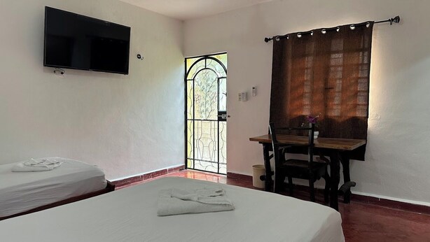 Habitación de hotel con dos camas, un televisor de pantalla plana, una mesa de comedor con sillas y una ventana con cortinas.