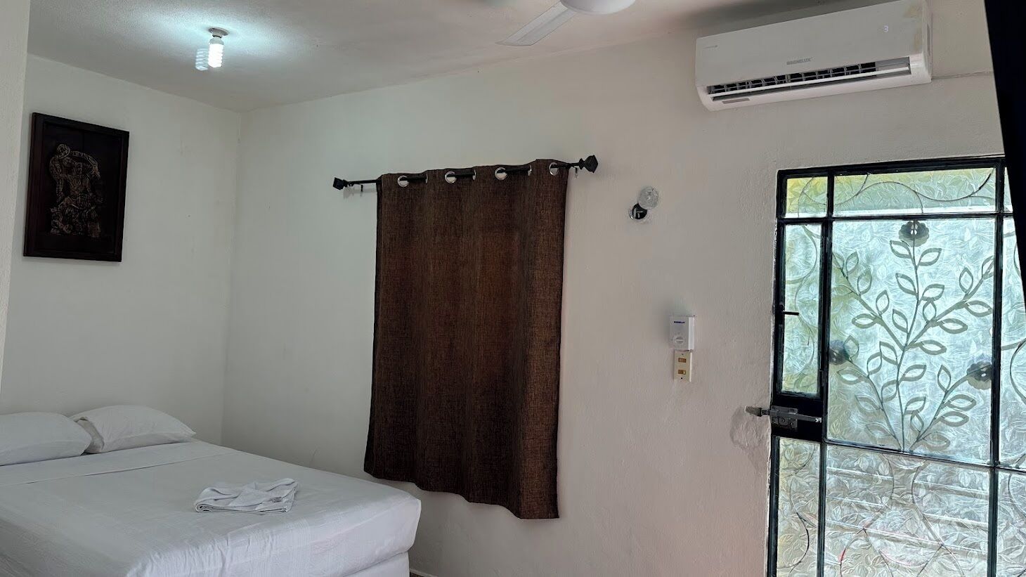 Una habitación con cama, ventana con vista decorativa, equipo de aire acondicionado y cortina.