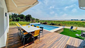 Uma área à beira da piscina com mesa e cadeiras, um espaço de estar coberto e vista para um campo.