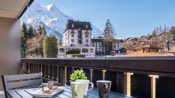 Un balcon avec une table dressée pour deux personnes, d’où l’on peut admirer une montagne et une ville.
