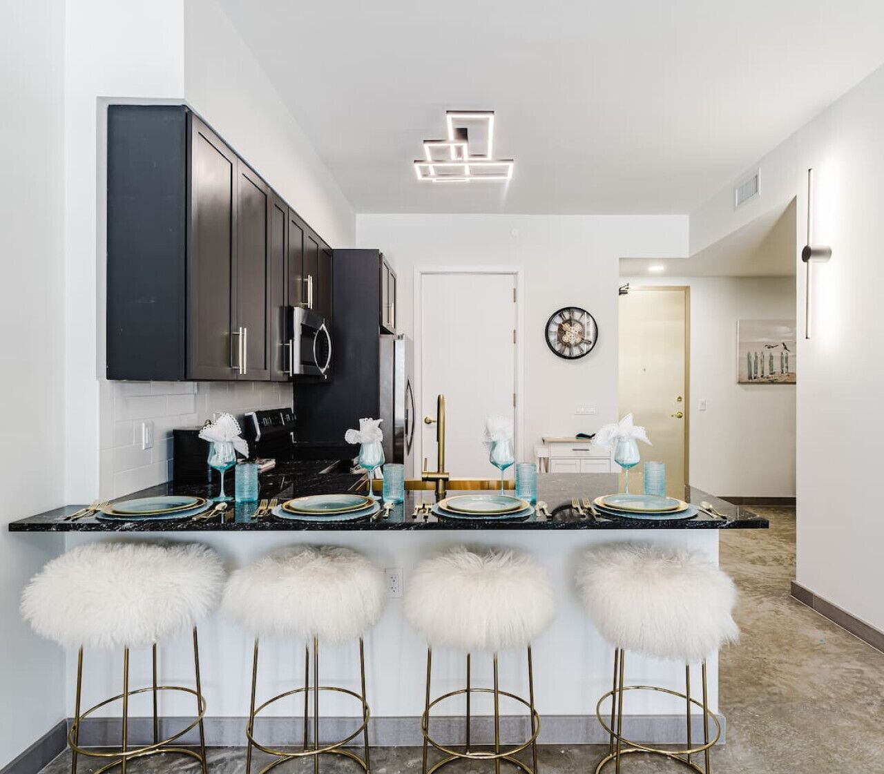 A modern kitchen with dark cabinets, a central island with bar stools, and a dining area with a white table and chairs.