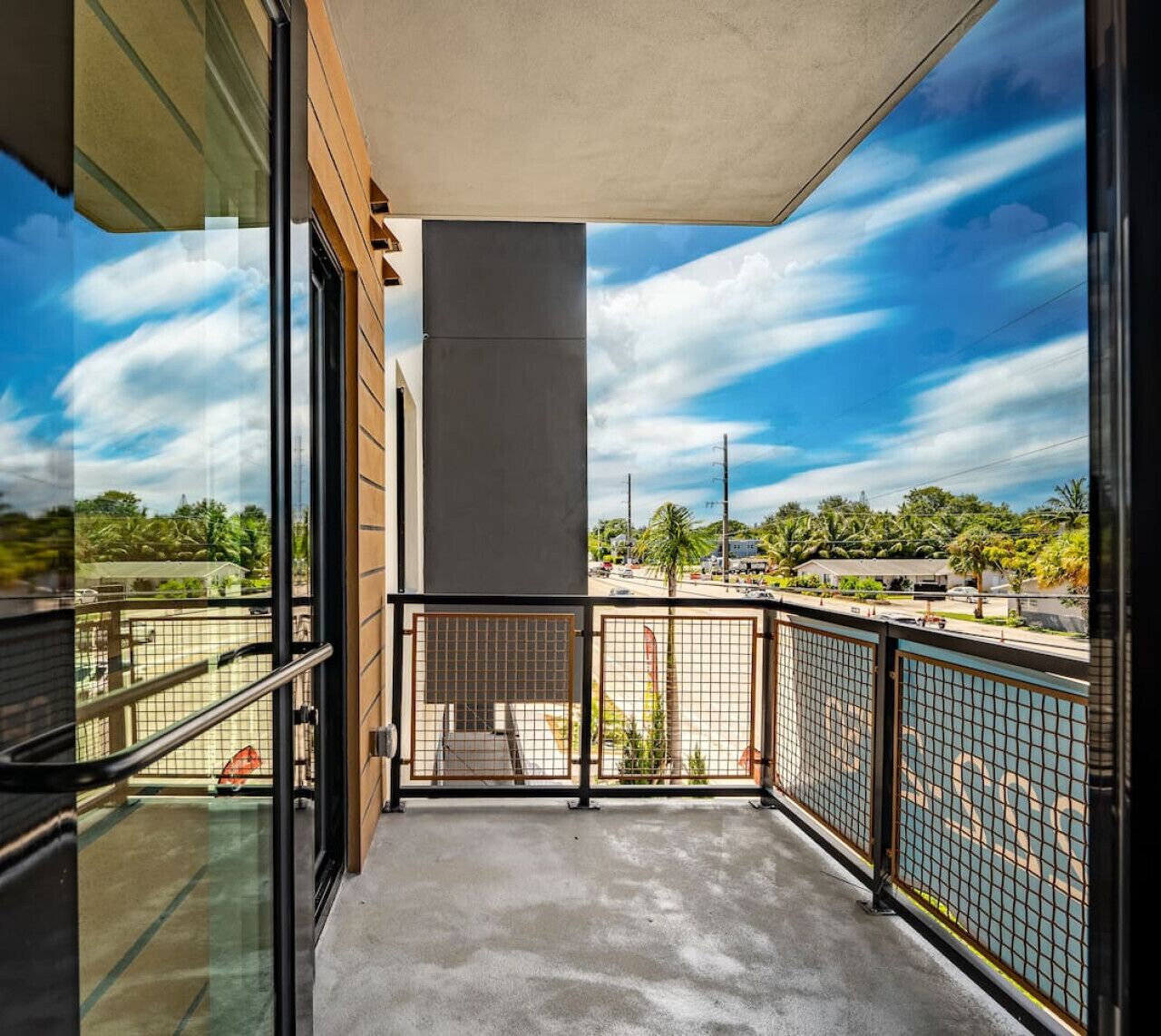 A balcony with a concrete floor, metal railing, and a view of a parking lot and trees.