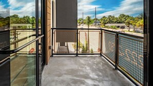 Ein Balkon mit Betonboden, Metallgeländer und Blick auf einen Parkplatz und Bäume.
