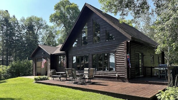 A log cabin with a deck, outdoor seating, and a flag.