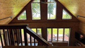 A wooden interior with a sloped ceiling, large windows, and a staircase.