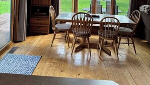 A wooden cabin with a dining area featuring a table and chairs, large windows, and a view of the outdoors.