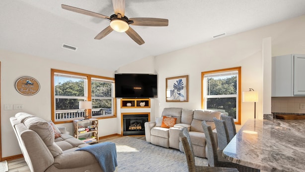 A spacious living room with a fireplace, comfortable seating, a flat-screen TV, and large windows offering a view of the outdoors. - Coastal Retreat with Beautiful views-completely updated for a cozy stay! (Kitty Hawk)