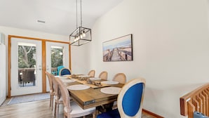 A dining area with a wooden table, blue upholstered chairs, and a hanging light fixture. - Coastal Retreat with Beautiful views-completely updated for a cozy stay! (Kitty Hawk)