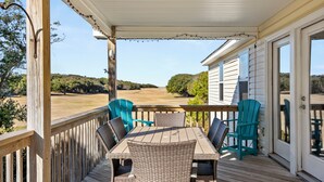 A covered outdoor deck with a table and chairs, overlooking a scenic landscape. - Coastal Retreat with Beautiful views-completely updated for a cozy stay! (Kitty Hawk)