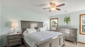 A bedroom with a bed, nightstands, a dresser, a ceiling fan, and a window with a view. - Coastal Retreat with Beautiful views-completely updated for a cozy stay! (Kitty Hawk)