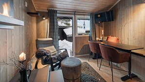 En mysig stuga med träpanel på insidan, en matplats med två stolar, ett bord och en öppen spis.