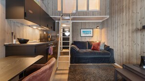 Ett kompakt kök med träinredning, en matplats med en bänk och ett mysigt vardagsrum med en soffa och en stege som leder upp till ett loft.