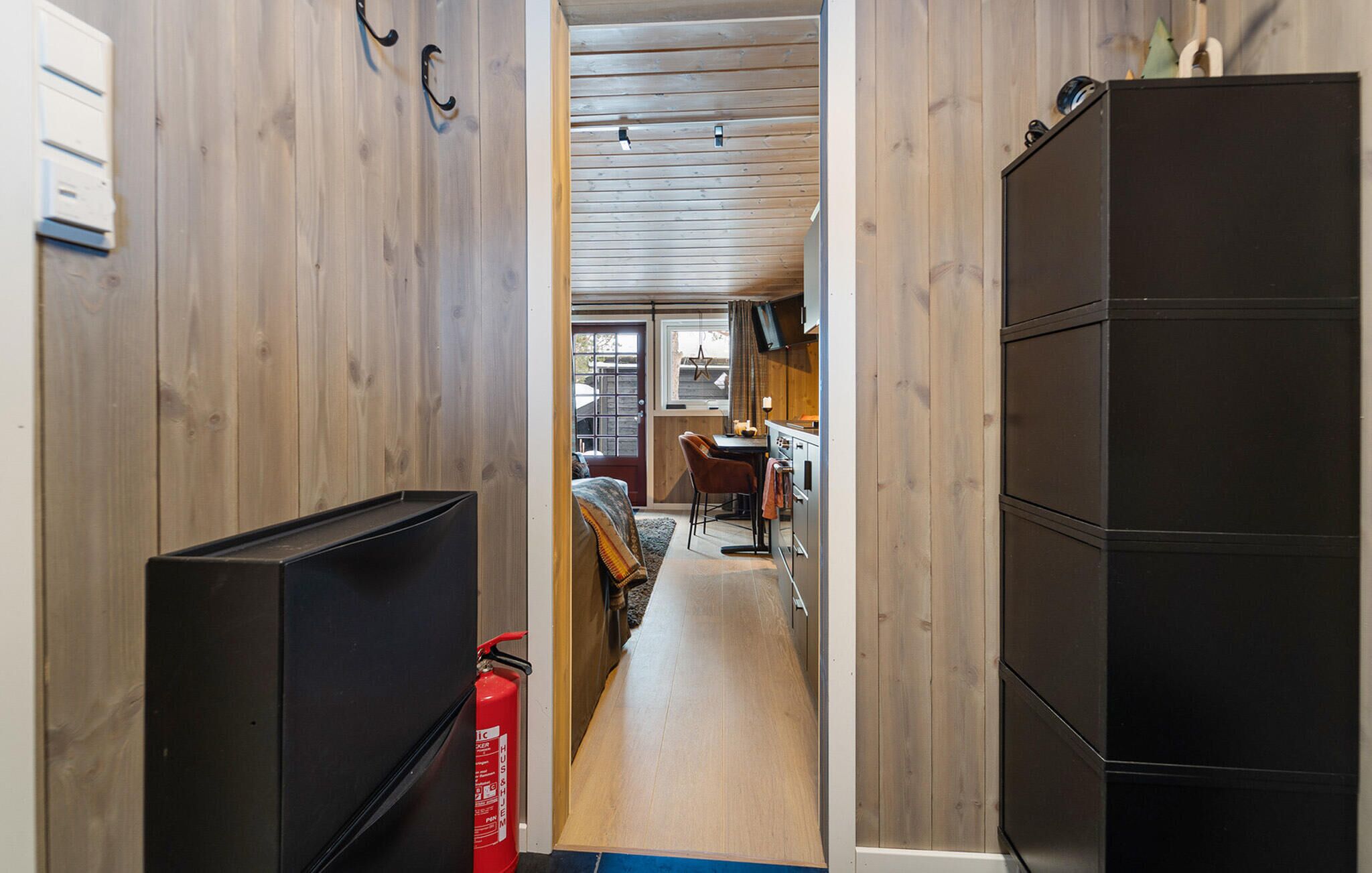 A narrow hallway with wooden walls, a black cabinet on the right, and a red fire extinguisher on the left.