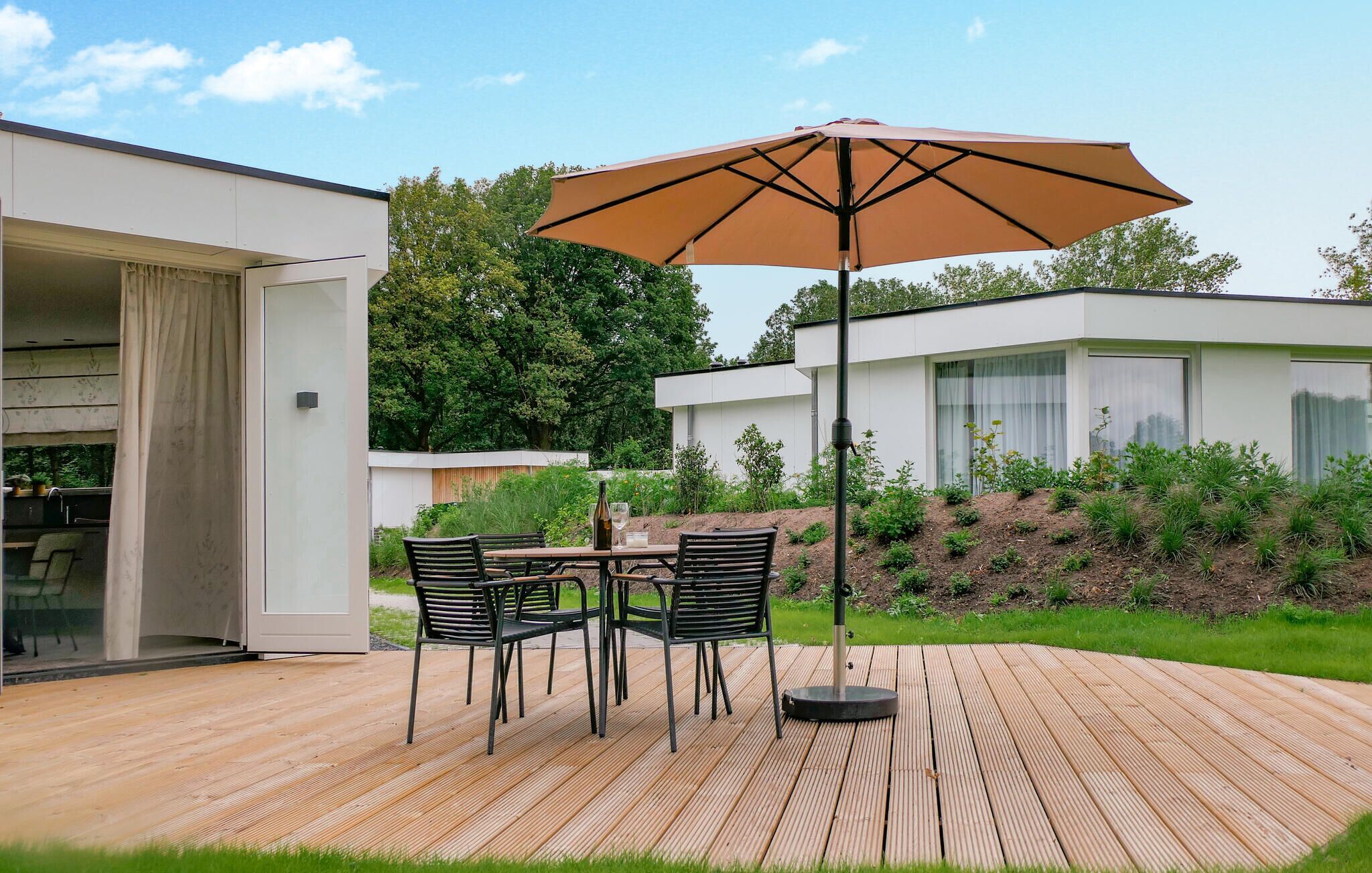 Une terrasse avec une plateforme en bois, une table entourée de chaises et un grand parasol.