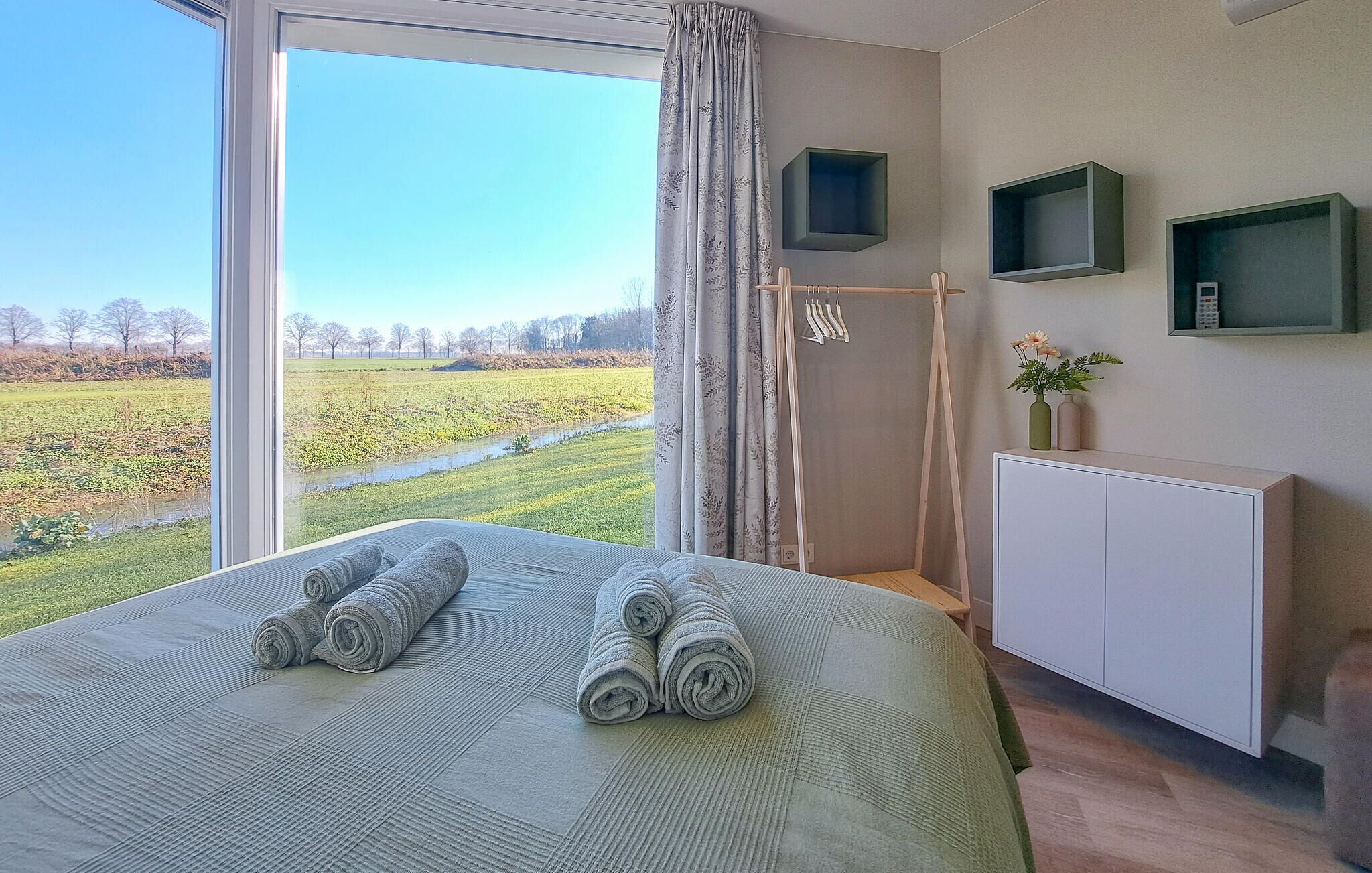 A bedroom with a large window, a bed with rolled towels, a radiator, and a small cabinet.
