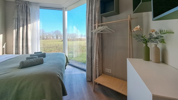 A modern bedroom with a large bed, a bench, a TV, and a view of a green field through the window. - 2 bedroom gorgeous home in Afferden (Afferden)