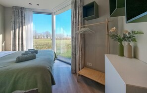 A modern bedroom with a large bed, a bench, a TV, and a view of a green field through the window. - 2 bedroom gorgeous home in Afferden (Afferden)
