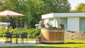 A patio with a table and chairs, a wooden planter, and a modern building in the background. - 2 bedroom gorgeous home in Afferden (Afferden)